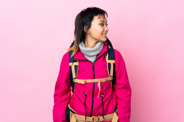 Foto junges bergsteigermädchen mit einem großen rucksack auf lokalisiertem rosa, das zur seite schaut