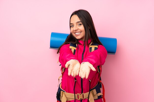 Junges Bergsteigermädchen mit einem großen Rucksack über isolierter rosa Wand, die imaginären Copyspace auf der Handfläche hält, um eine Anzeige einzufügen