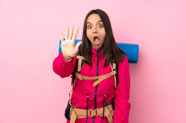 Junges Bergsteigermädchen mit einem großen Rucksack über rosa, der fünf mit den Fingern zählt