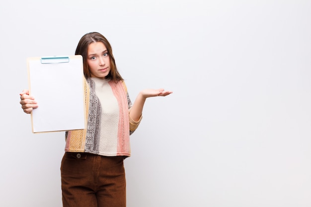 Junges blondes hübsches Mädchen mit einem Papierblatt gegen weiße Wand