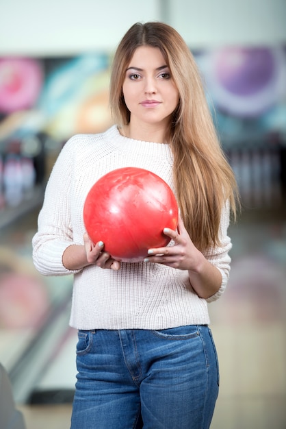 Junges blondes lächelndes Mädchen, das Bowlingspiel spielt.