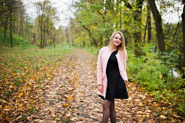 Junges blondes Mädchen im rosafarbenen Mantel posierte im Herbstpark