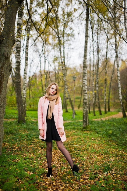 Junges blondes Mädchen im rosafarbenen Mantel posierte im Herbstpark