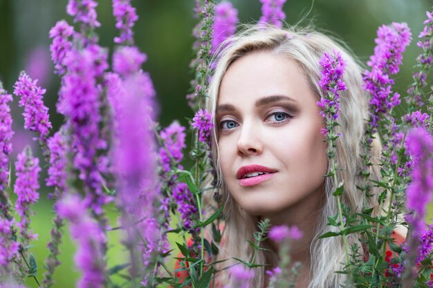 Junges blondes Mädchen in den Büschen der purpurroten Blumen. Nahansicht.