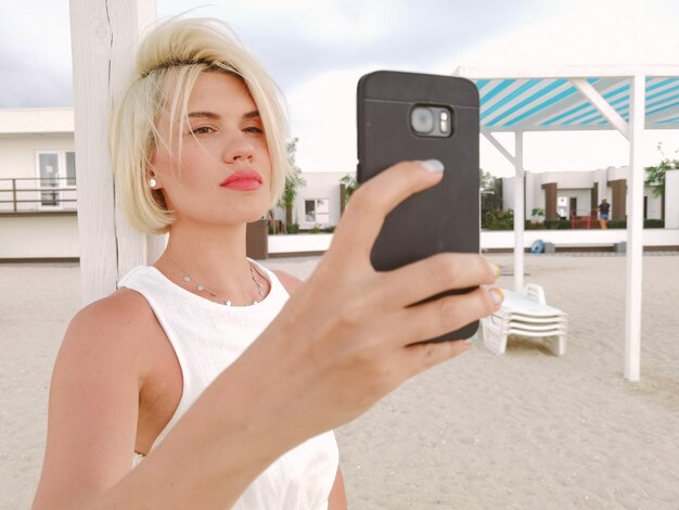 Junges blondes Mädchen macht Selfie mit dem Smartphone am Strand