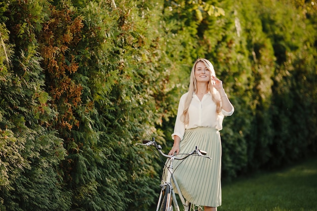 junges blondes Mädchen mit dem langen Haar, das nahes Weinleseweißfahrrad steht.