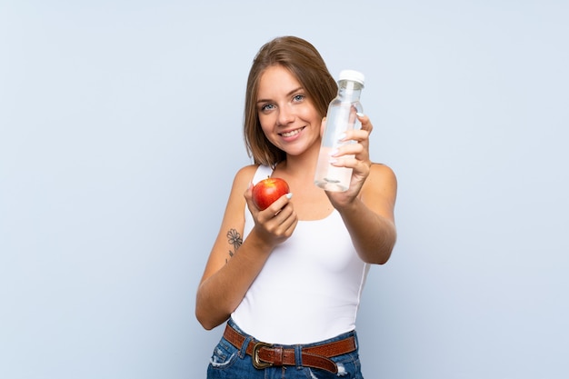 Junges blondes Mädchen mit einem Apfel und mit einer Flasche Wasser über lokalisierter Wand