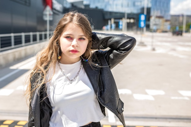 Junges blondes Schulmädchen in schwarzer Lederjacke posiert auf dem Parkplatz