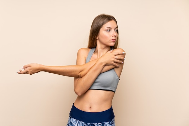 Junges blondes Sportmädchen über dem lokalisierten Hintergrund, der Arm ausdehnt