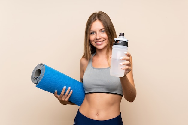 Junges blondes Sportmädchen über lokalisierter Wand mit Sportwasserflasche und mit einer Matte