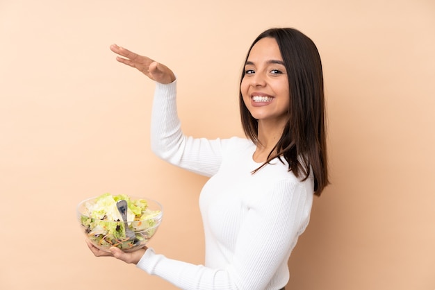 Junges brünettes Mädchen, das einen Salat über isoliertem Hintergrund hält, der copyspace hält, um eine Anzeige einzufügen