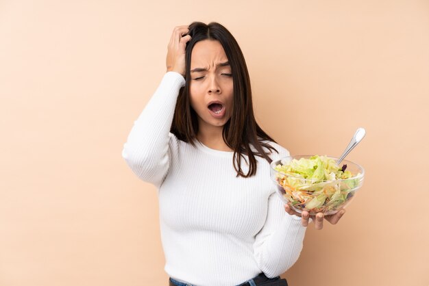 Junges brünettes Mädchen, das einen Salat über isoliertem Hintergrundgähnen hält