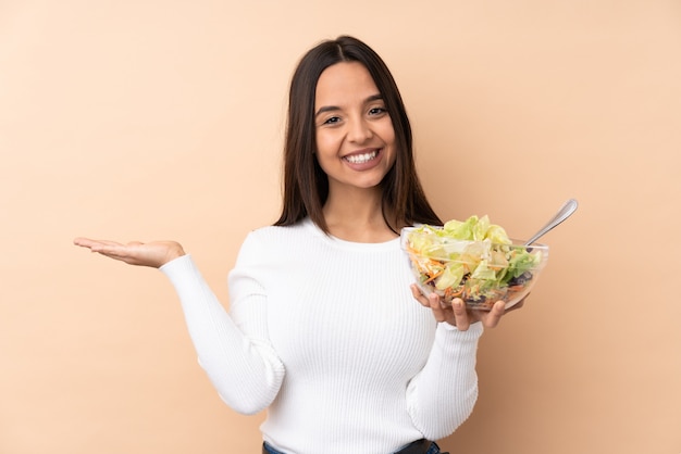 Junges brünettes Mädchen, das einen Salat über isolierter Wand hält, die imaginären Copyspace auf der Handfläche hält, um eine Anzeige einzufügen
