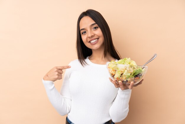 Junges brünettes Mädchen, das einen Salat über isolierter Wand stolz und selbstzufrieden hält