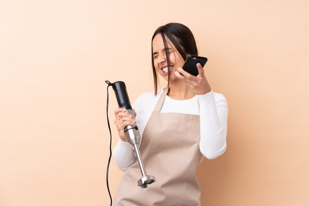 Junges brünettes Mädchen, das Stabmixer mit Telefon in der Siegposition übergibt