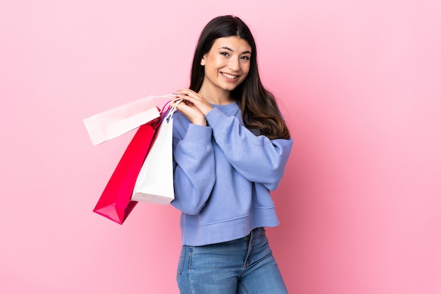 Junges brünettes Mädchen über rosa Wand, die Einkaufstaschen hält