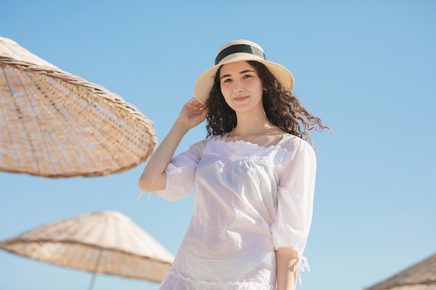 Foto junges brünettes teenager-mädchen mit lockigem haar und strohhut, das an sonnigen tagen an der küste bleibt