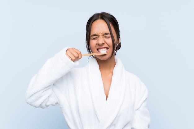 Junges Brunettemädchen im Bademantel mit Make-up über lokalisierter blauer Wand