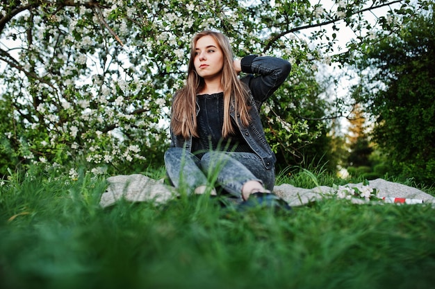 Junges Brunettemädchen in den Jeans, die auf Plaid gegen Frühlingsblütenbaum sitzen