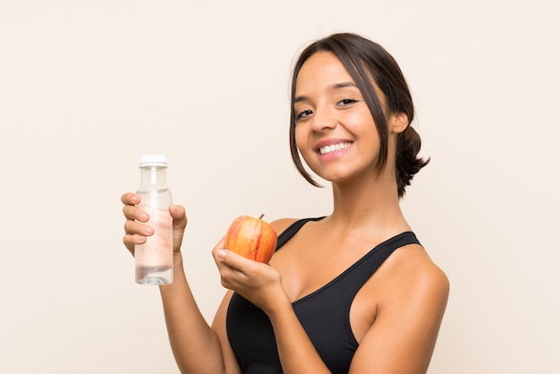 Junges Brunettemädchen mit einem Apfel und mit einer Flasche Wasser über lokalisierter Wand