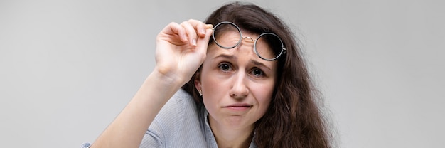 Junges Brunettemädchen mit Gläsern. Sie hob die Brille.