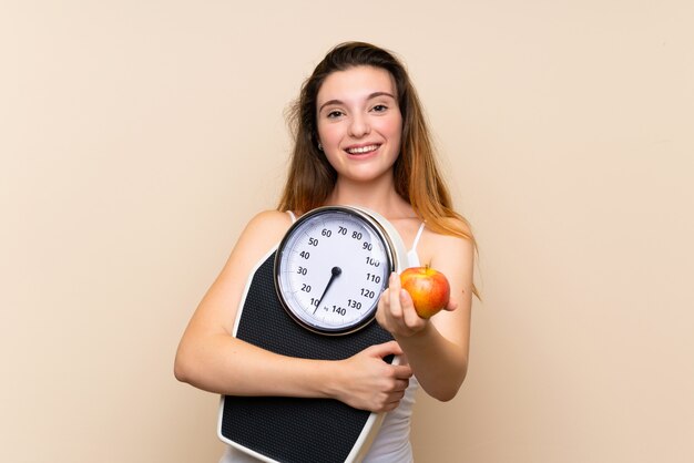 Junges Brunettemädchen mit Waage und mit einem Apfel über lokalisierter Wand