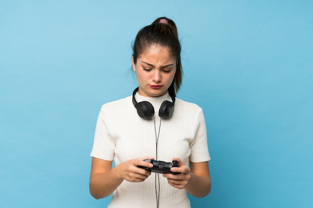 Junges brunettemädchen über dem lokalisierten blau, das an den videospielen spielt