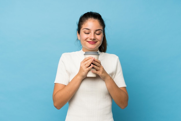 Junges Brunettemädchen über lokalisiertem blauem haltenem Kaffee zum Mitnehmen