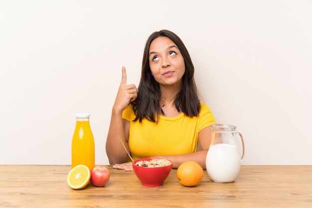 Junges Brunettemädchen, welches die Frühstücksmilch zeigt mit dem Zeigefinger hat