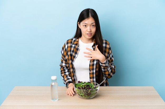 Junges chinesisches Mädchen, das einen Salat isst, der auf sich selbst zeigt