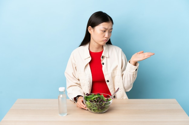 Junges chinesisches Mädchen, das einen Salat isst, der Copyspace mit Zweifeln hält