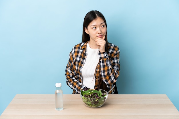 Junges chinesisches Mädchen, das einen Salat isst, der eine Idee denkt, während sie aufschaut