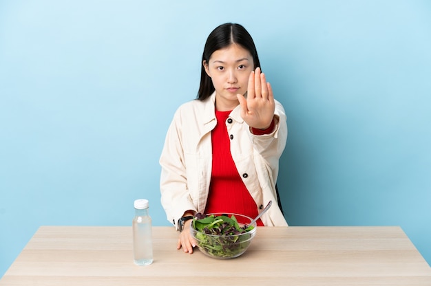 Junges chinesisches Mädchen, das einen Salat macht, der Stoppgeste macht