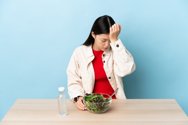 Junges chinesisches Mädchen, das einen Salat mit Kopfschmerzen isst