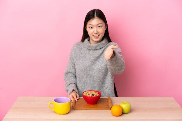 Junges chinesisches Mädchen, das Frühstück in einem Tisch Händeschütteln für das Schließen eines guten Geschäfts hat