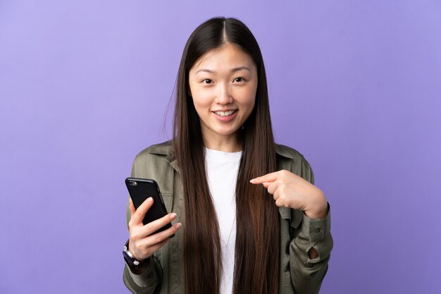 Junges chinesisches Mädchen, das Handy über lila mit überraschendem Gesichtsausdruck verwendet