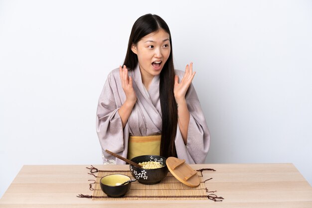 Junges chinesisches Mädchen, das Kimono trägt und Nudeln mit überraschendem Gesichtsausdruck isst