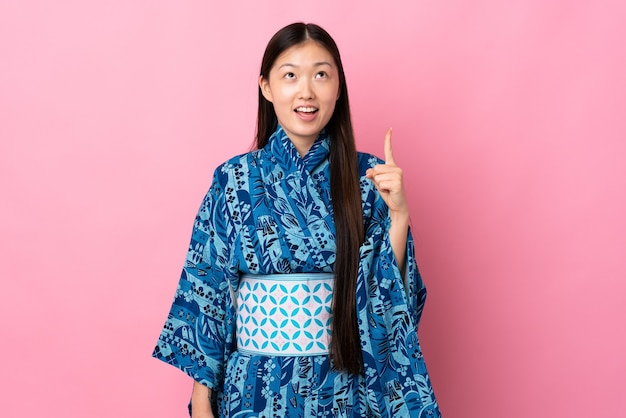 Junges chinesisches Mädchen, das Kimono über lokalisiertem Hintergrund trägt, der oben und überrascht zeigt