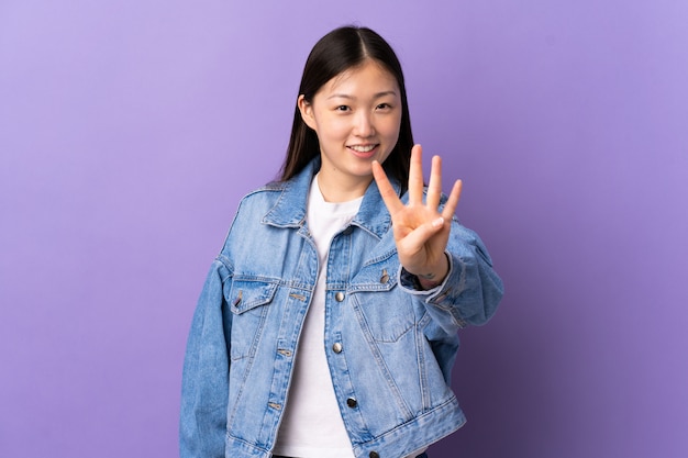 Junges chinesisches Mädchen über isoliertem Purpur glücklich und zählt vier mit den Fingern