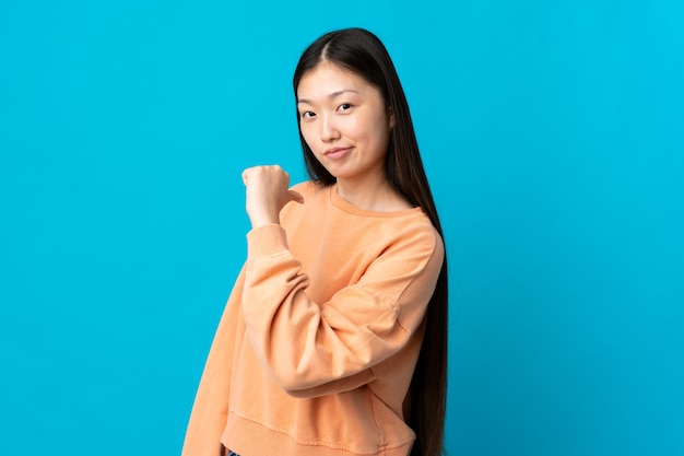 Junges chinesisches Mädchen über isolierter blauer Wand stolz und selbstzufrieden