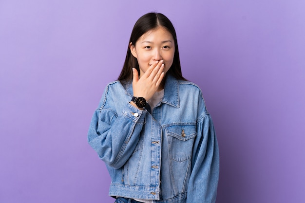 Junges chinesisches Mädchen über lila Wand glücklich und lächelnd, das Mund mit Hand bedeckt