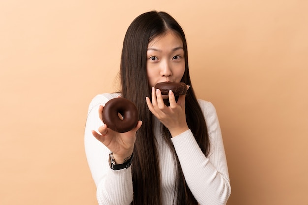 Junges chinesisches Mädchen über lokalisiertem Hintergrund, der einen Donut hält