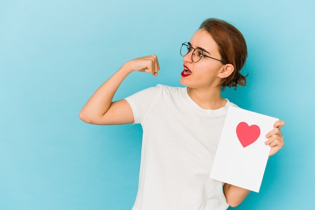 Junges dünnes arabisches Mädchen, das eine Valentinstagskarte hält, die Faust nach einem Sieg, Gewinnerkonzept erhebt.