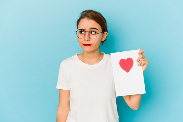 Junges dünnes arabisches Mädchen, das eine Valentinstagskarte verwirrt hält, fühlt sich zweifelhaft und unsicher.