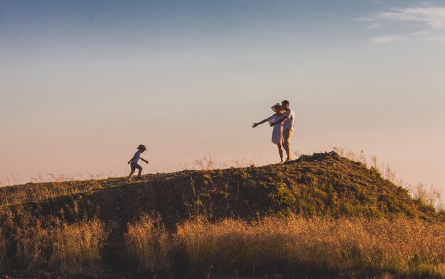 Junges Ehepaar, das auf seinen kleinen Sohn wartet, um zu kommen Vorschuljunge, der den Hügel hinauf zu den Eltern geht Einladung, sich der Familie anzuschließen Paar, das darauf wartet, dass sein Kind kommt Adoptionskonzept