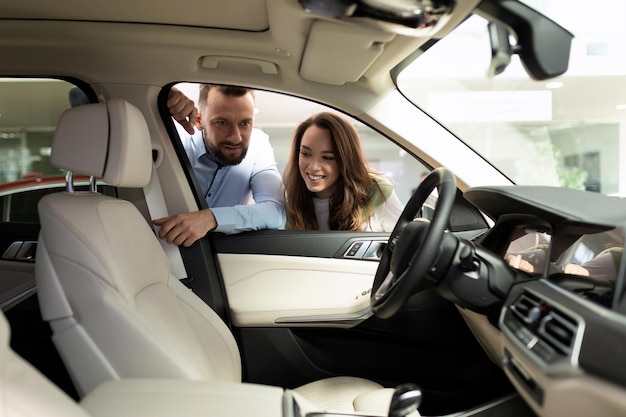 Junges Ehepaar, das die Eigenschaften eines neuen Autos in einem Autohaus studiert