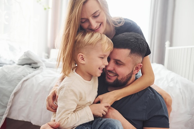 Junges Ehepaar mit ihrem kleinen Sohn hat tagsüber gemeinsame Freizeit im Schlafzimmer.