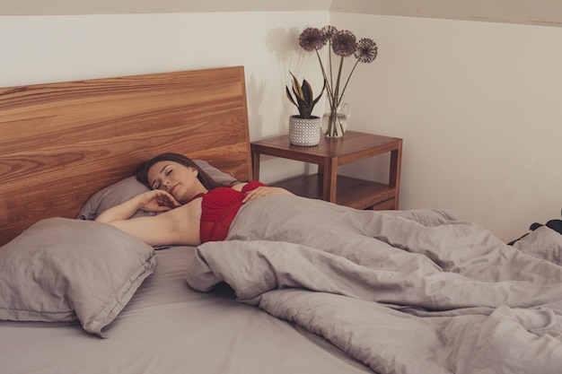 Junges erwachsenes Mädchen versteckt sich im Bett unter der Decke