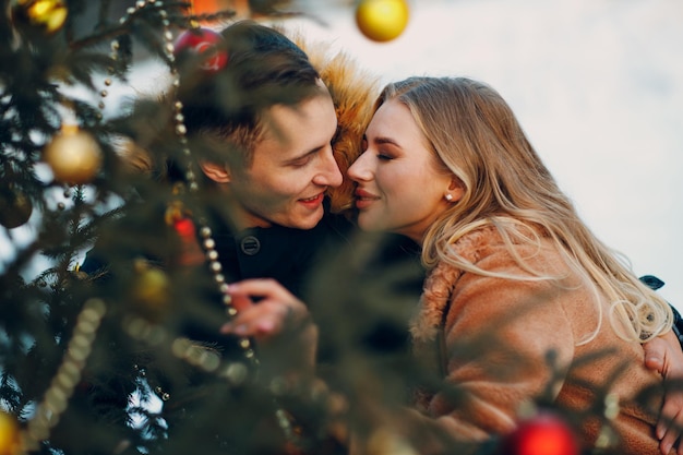 Junges erwachsenes Paar küssen, während Weihnachtsbaum im Winterwald verziert. Neujahrsfeier Konzept für Kiefernferien