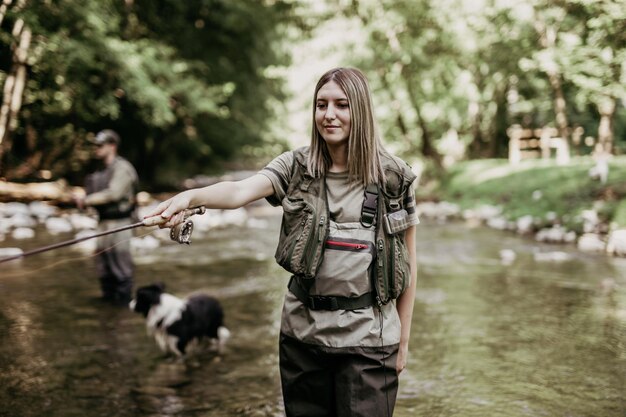 Junges erwachsenes Paar mit Hund fischt zusammen auf schnellem Gebirgsfluss. Konzept für aktive Menschen und Sportfliegenfischen.